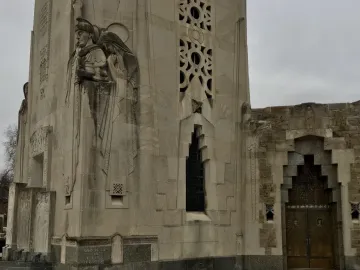 Relief carvings and decorative stonework on the National Shrine of the Little Flower tower, with a bronze double door in a stepped archway.