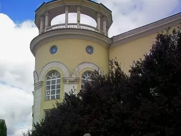 The Shot in the Back monument showing two embracing figures on a dark base with a wreath, set among trees with a towered building behind it.