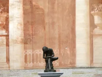 Boy with Thorn sculpture of a kneeling boy examining his raised foot on a marble pedestal.