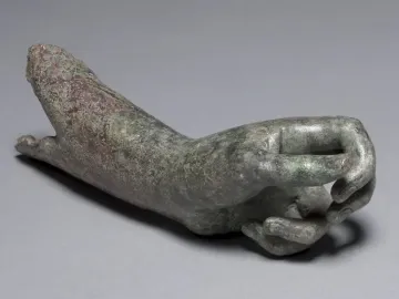 Detached bronze hand and forearm from the Cleveland Apollo, with a green and reddish-brown patina and curled fingers.