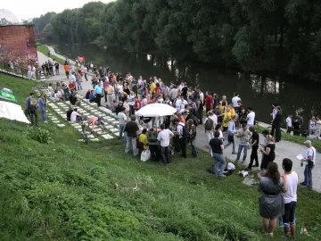 Crowd gathered around the Keyboard Monument, a land-art installation made of rectangular blocks on a grassy slope beside the river.