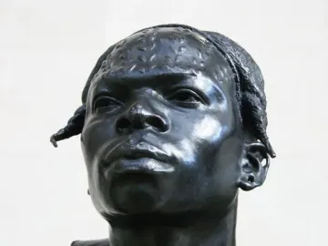 Dark metallic bust of an Aruwimi native with textured hair, a prominent nose, and an earring on a square base.