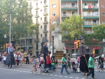 The Fountain of Hercules stands in a city square with oversized costumed figures and pedestrians around the base.