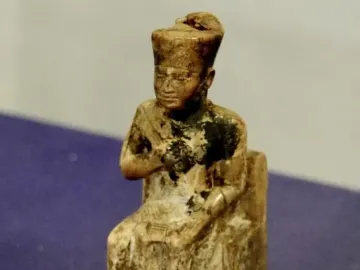 Khufu statuette showing a seated figure wearing a tall rectangular headdress on a clear base.