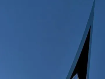 The Life Electric sculpture in Como, a tall reflective silver monument against a deep blue twilight sky and waterfront lights.