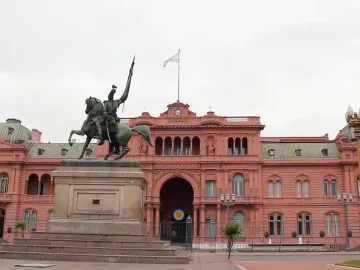 Manuel Belgrano equestrian monument with a rearing horse and raised standard in front of a pink government building.