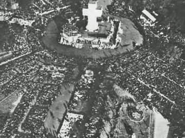 A large crowd gathers around the Monument to the Carta Magna and Four Regions of Argentina, with a tall cross rising from the top of the monument.