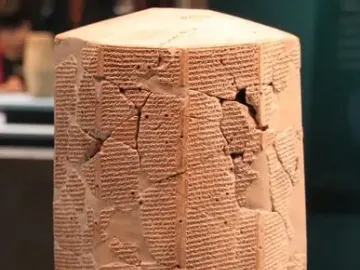 Rassam cylinder covered with dense rows of cuneiform script on a reddish-brown multi-sided prism with visible cracks and missing fragments.