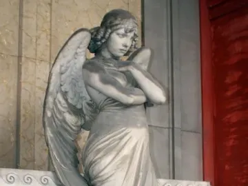 Monteverde Angel marble sculpture of a winged angel with folded arms and bowed head beside inscribed grave panels.