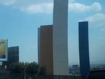 Torres de Satélite with three tall colored rectangular towers against a partly cloudy blue sky.