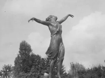 The Dancing Girl statue on a pedestal outdoors, with a man standing near the base among greenery.