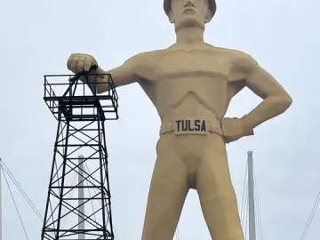 Golden Driller statue standing beside an oil derrick model in Tulsa
