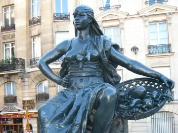L\'Afrique by Eugène Delaplanche, a dark statue of a seated woman with a headwrap holding a basket of fruit, with one foot resting on a turtle.