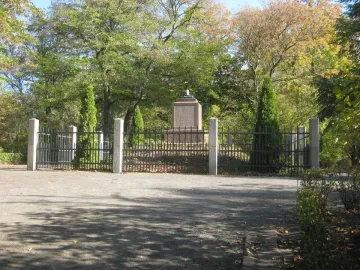 Napoleonstein stone pillar behind a black metal fence in a sunny park.