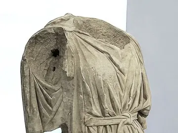 Heavily damaged headless and armless torso of Athena and Marsyas, displayed on metal supports in a museum.