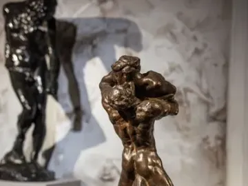 Je suis belle bronze sculpture showing two intertwined muscular figures on a rough base.