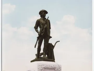 The Minute Man bronze statue of a colonial militiaman holding a musket beside a plow on a stone pedestal in a park.