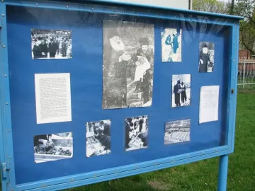 Blue display board for the Monument of Common Martyrdom, covered with historical photographs and text documents.