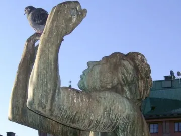 Close-up of the Orpheus Fountain bronze statue with a pigeon perched on its raised hand.