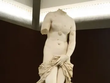 Headless marble Venus Landolina statue with one arm missing, draped cloth around her lower body, standing on a pedestal with an information plaque.