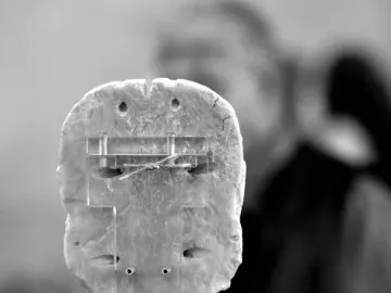 Back view of the Warka Mask on a display stand with acrylic supports and visible repairs.