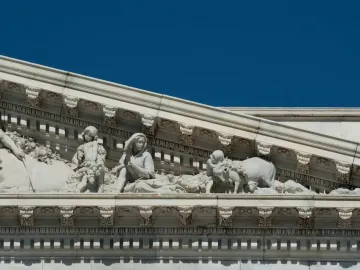 Apotheosis of Democracy pediment relief showing carved figures with livestock, a child carrying grapes, and a seated woman under a blue sky.