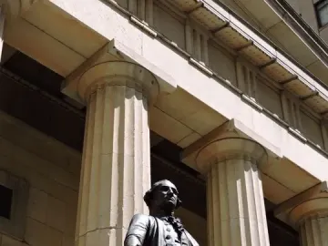 The Statue of George Washington stands on a stone platform before a classical building with tall fluted columns.
