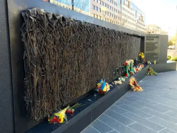 Holodomor Memorial bronze wall with a relief of wheat stalks, flowers, candles, and small Ukrainian flags at the base.