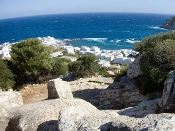 The Kouros of Apollonas lies unfinished in a rocky quarry overlooking the sea and coastal buildings.