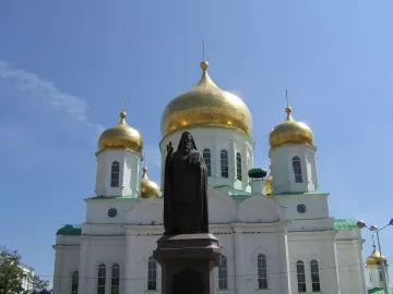 Monument to Dimitry of Rostov in front of a white cathedral with golden domes and crosses.