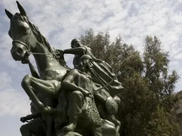 Low-angle view of the Saladin equestrian statue, showing a bronze warrior on a rearing horse above smaller figures on a rock-like base.
