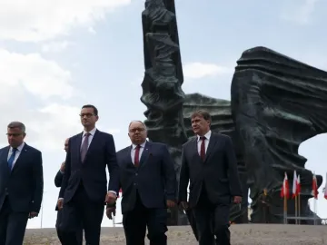 The Silesian Insurgents\' Monument rises behind a group of men in dark suits, with Polish flags near its base.