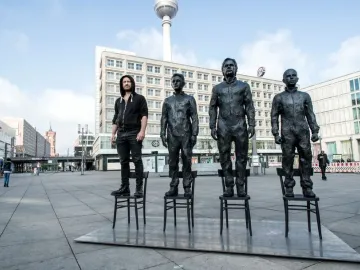 Anything To Say? sculpture with three dark statues and one person standing on chairs in a city plaza