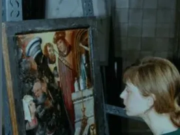 A conservator examines the Fisenne Altarpiece while holding a brush and palette beside the painted carved panel.