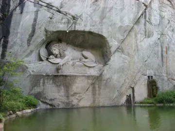 The Lion Monument shows a dying lion carved into a rock grotto, pierced by a spear, with inscriptions above and below and water in front.