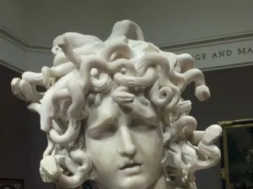 Bernini\'s Medusa marble bust with snake-like hair and a sorrowful expression in a museum gallery.