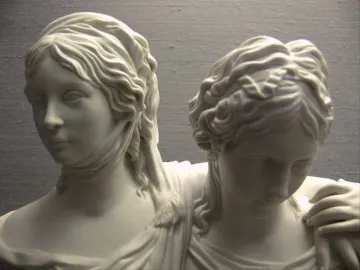 Close-up of the Princesses Monument showing two young women in a white sculpture, one facing forward and the other leaning in with her head lowered.