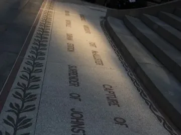 Granite paving with an engraved historical inscription beside the Sherman Monument, with a leaf pattern border and stone steps at right.