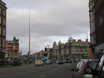 The Spire rises above Dublin street buildings under an overcast sky.