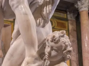 Marble sculpture detail of Ascanius beside the leg of Aeneas, holding a small vessel and looking upward.