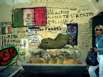 The Babuino Fountain, a weathered reclining stone statue with water flowing into a basin against a graffiti-covered wall.