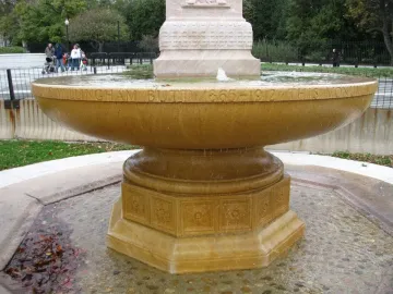 Butt–Millet Memorial Fountain with a shallow stone bowl, carved inscriptions, and an octagonal base in a pebbled basin.