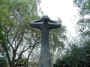 Der Mahner, a tall abstract bronze sculpture with upward-curving forms in a grassy park, with a plaque in front.