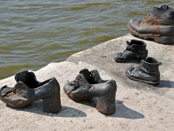 Metal shoes from the Shoes on the Danube Bank memorial on a concrete riverbank with calm water behind them.
