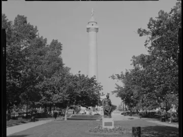Washington Monument rises above a park with trees, lawns, paths, and a seated statue in the foreground.
