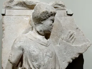 Damaged marble relief from the Bassae Frieze showing the upper body of a draped figure and a carved hand on the right.