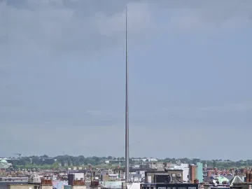 The Spire rises above Dublin rooftops and buildings under a cloudy sky.