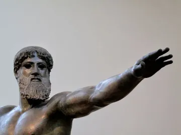 Artemision Bronze showing the upper torso and head of a bronze bearded man with curly hair and an extended arm.