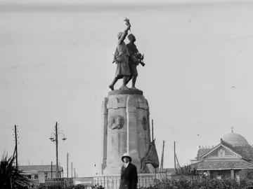 Demba et Dupont monument with two armed figures on a tall stone pedestal in a park-like square.
