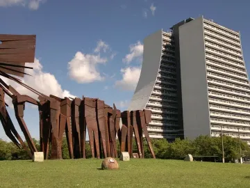 Monument to the Azoreans, a weathered steel abstract sculpture on a green lawn with a modern curved building behind it.